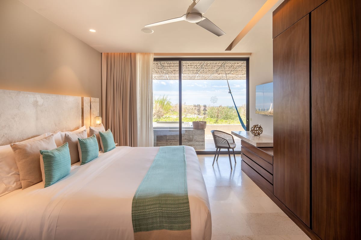 A modern hotel room with a large bed, a ceiling fan, a TV, and a view of the outdoors.