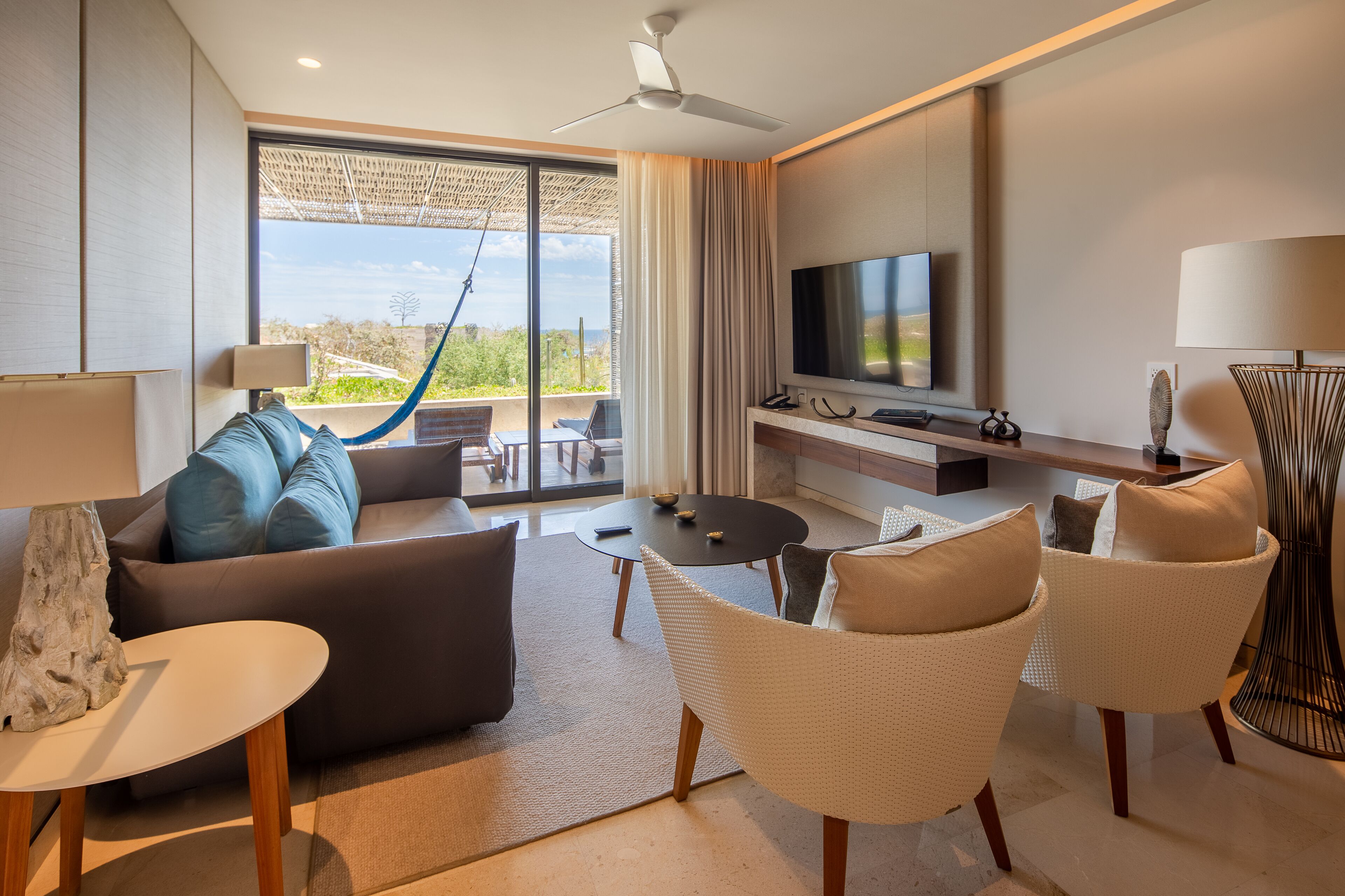 Un salon moderne avec un canapé, des fauteuils, un téléviseur et un balcon offrant une vue agréable.