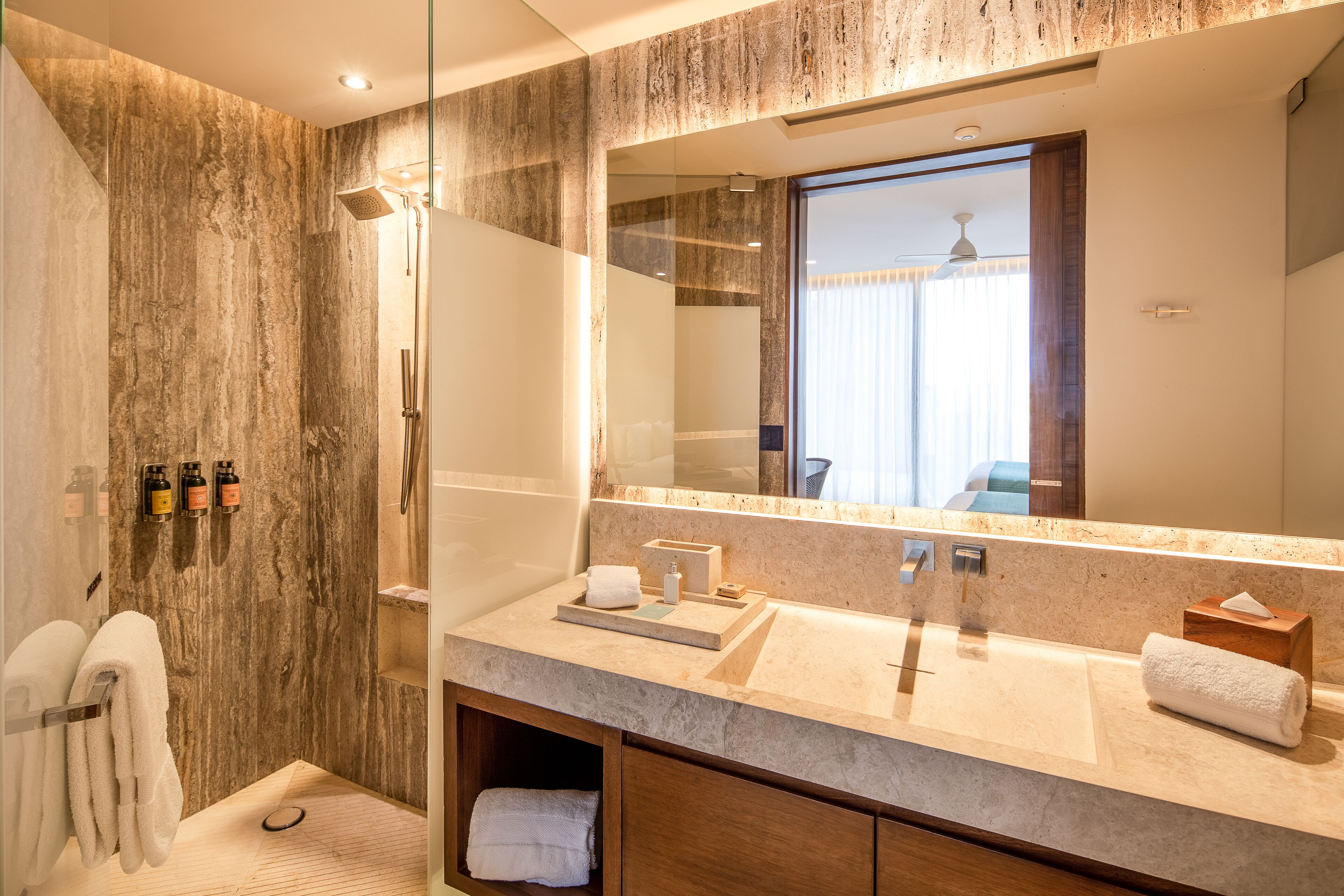 Un baño moderno con ducha de vidrio, un espejo grande y un lavabo con toallero.