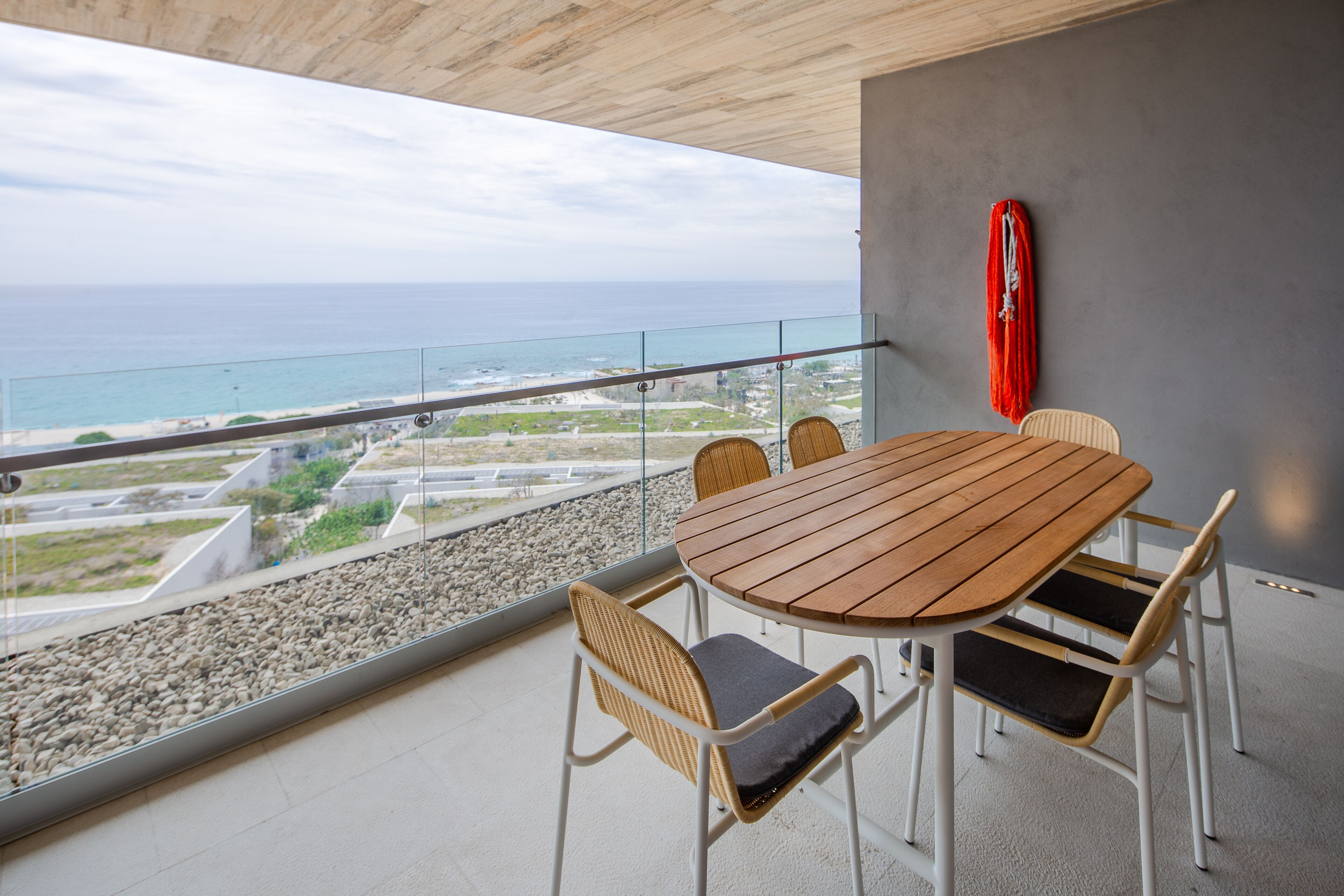 Un balcon avec une table en bois et des chaises en osier, donnant sur une plage et l’océan.