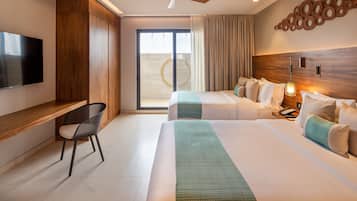 A hotel room with two beds, a desk, a chair, a TV, and a ceiling fan.