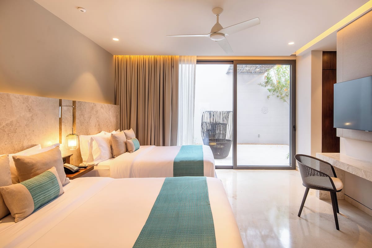 A hotel room with two beds, a TV, a ceiling fan, and a balcony with a chair.
