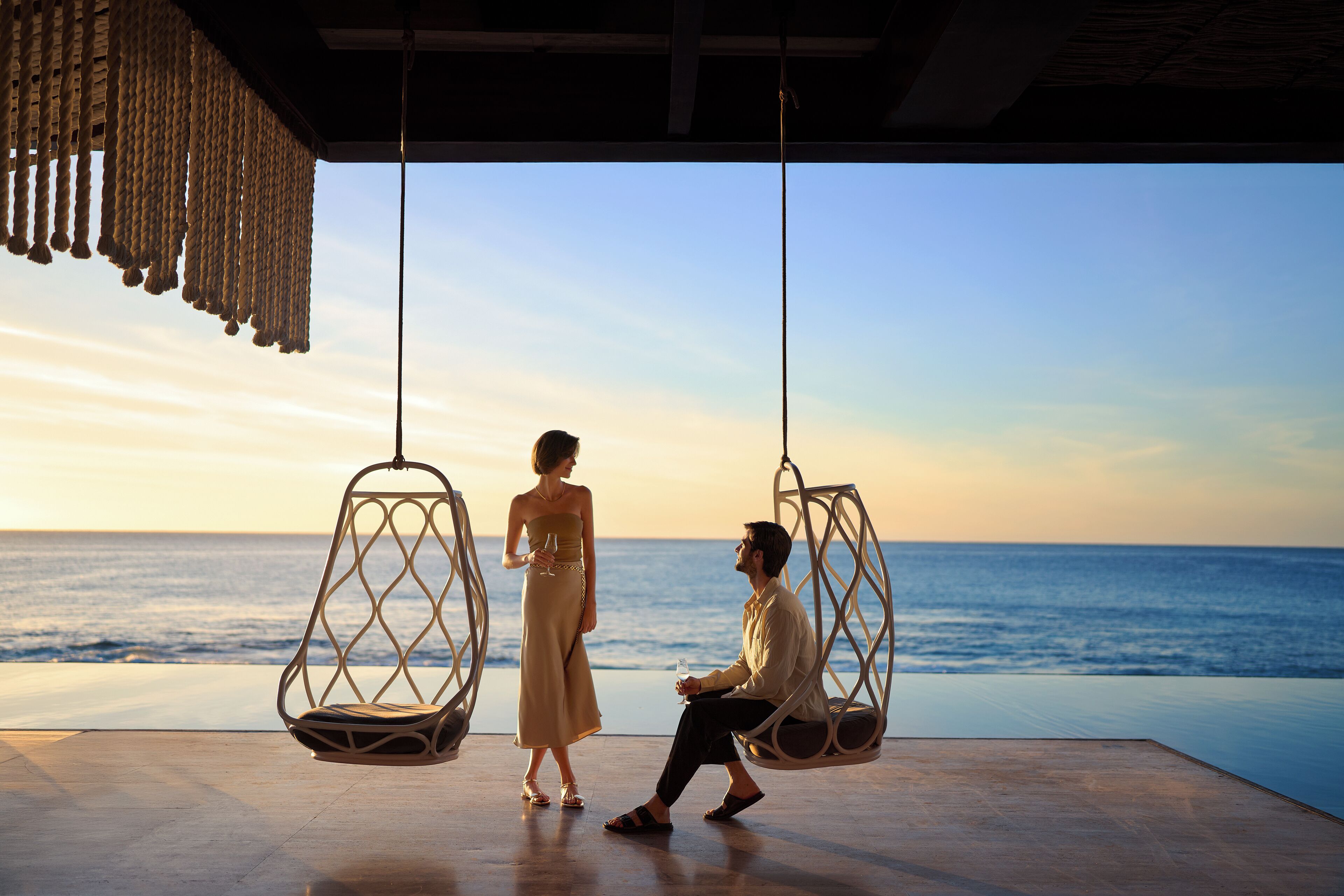 Una pareja en una silla colgante con vista al océano.