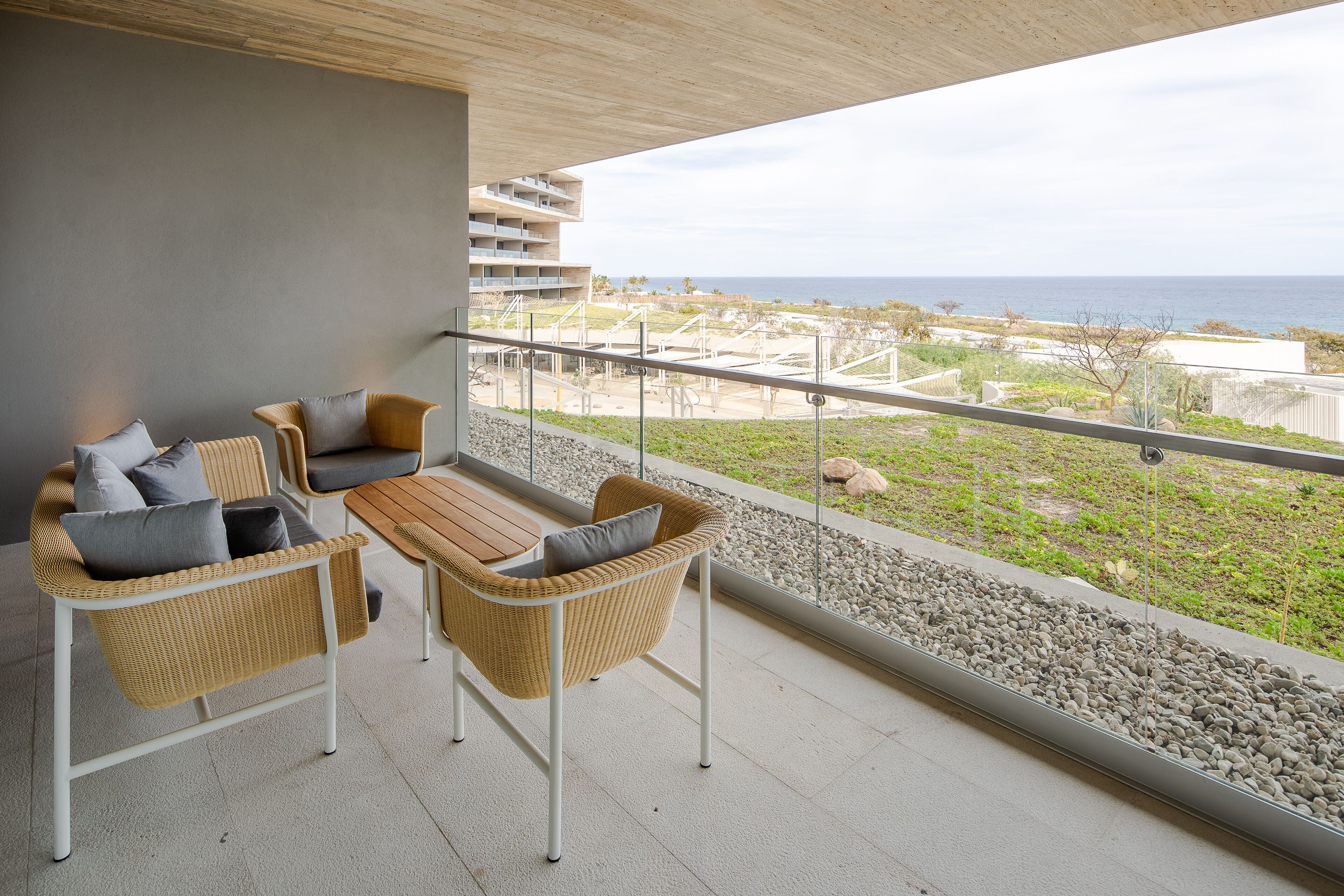 A balcony with wicker furniture, a view of the ocean, and a building in the background.