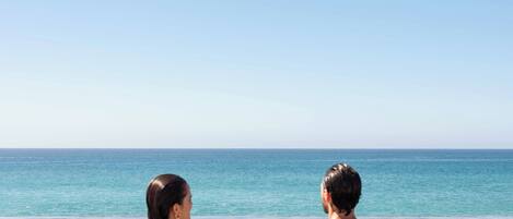 A couple holding hands in shallow water with a clear view of the ocean and sky.