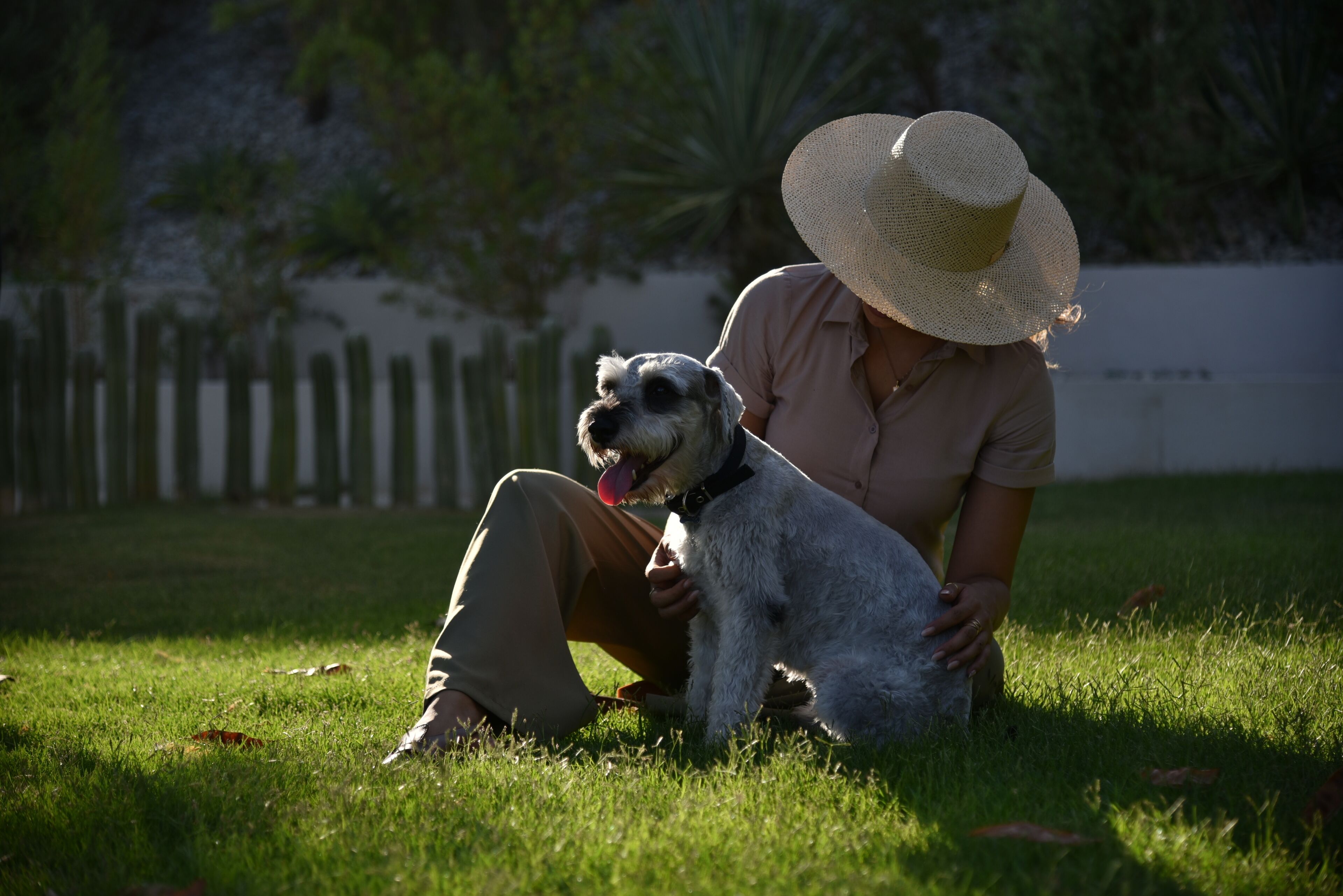 Eine Person sitzt mit einem Hund im Gras, eine Mütze tragend.