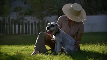 A person sitting on grass with a dog, wearing a hat.