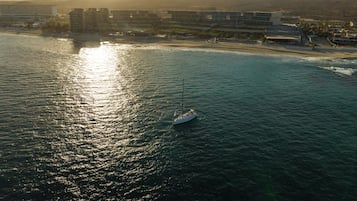 A coastal hotel with multiple buildings, a beach, and a sailboat in the water.