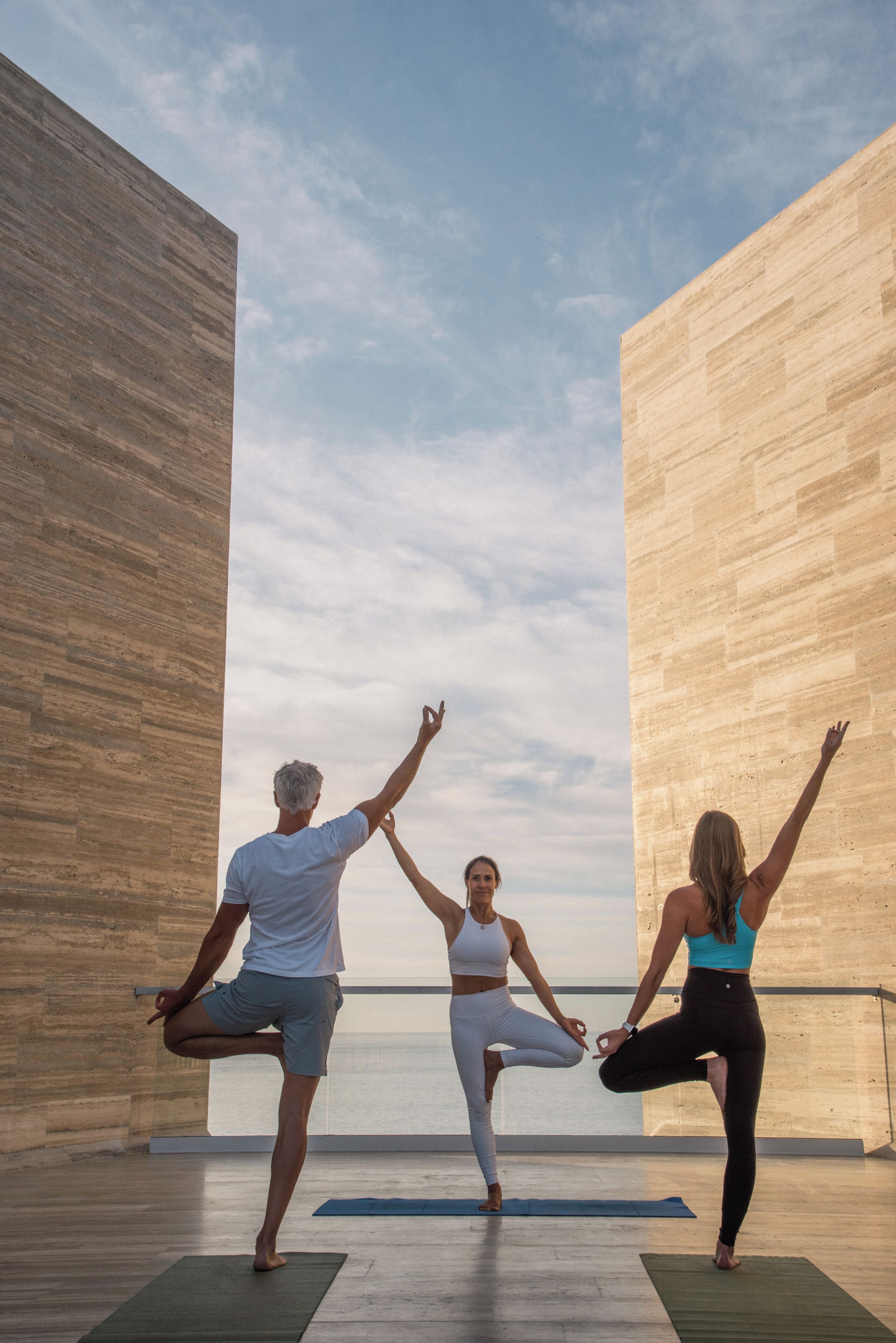 Tres personas practicando yoga en una habitación con paredes de madera y vistas al cielo.