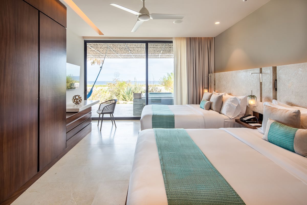 A modern hotel room with two beds, a desk, and a view of the ocean.