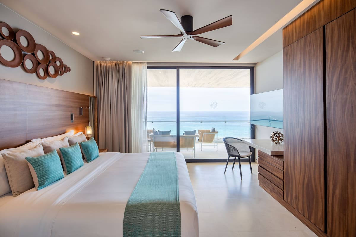 A modern hotel room with a large bed, a desk, and a view of the ocean.