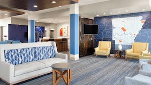 A lobby with a sofa, chairs, a small table, a map wall, and a TV. - Holiday Inn Express and Suites West Memphis by IHG (West Memphis)