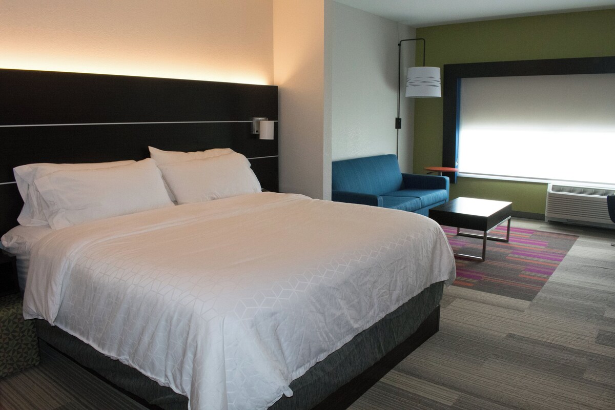 A hotel room with a large bed, a blue sofa, a small table, and a large window.