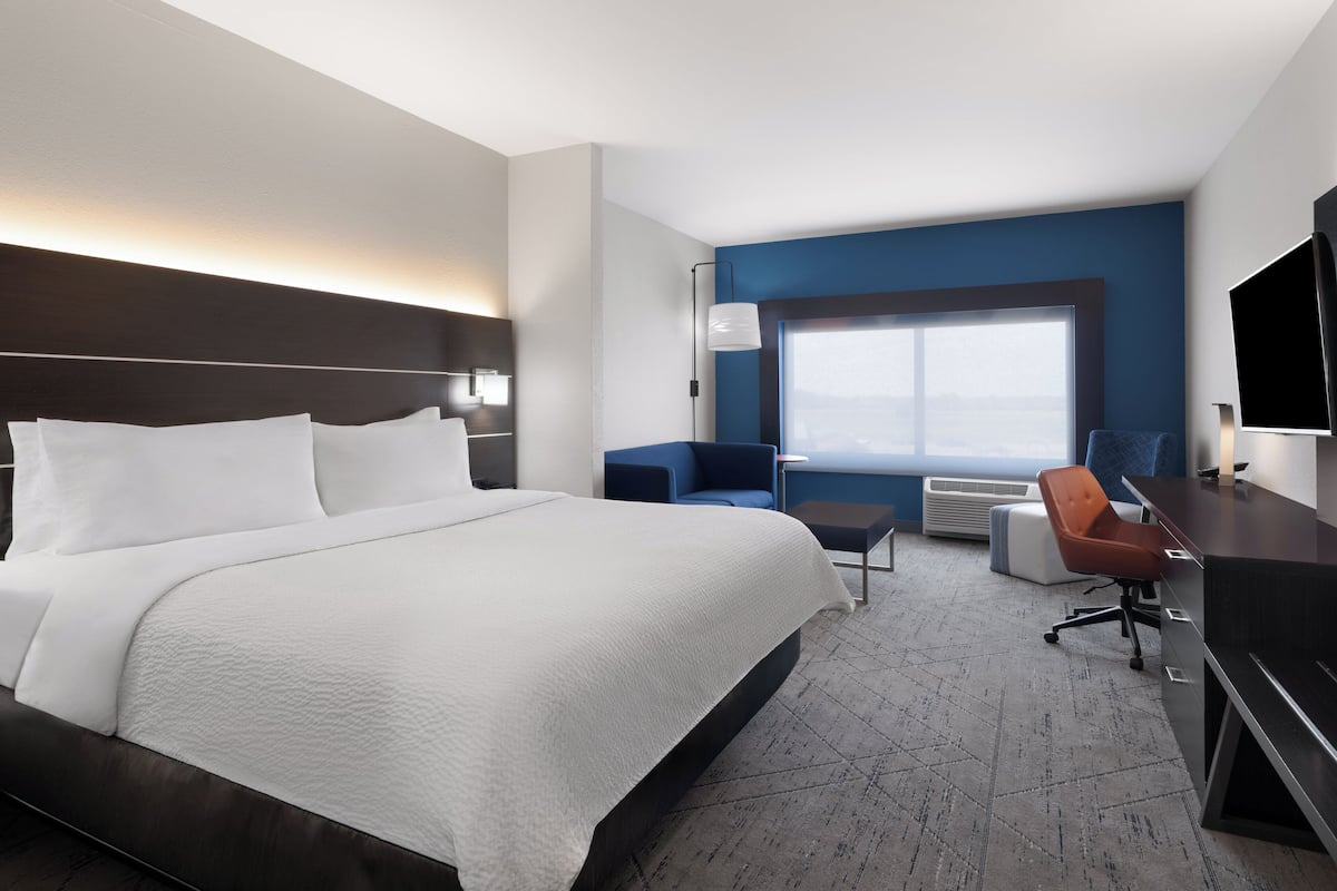 A modern hotel room with a large bed, a desk, a chair, and a TV.