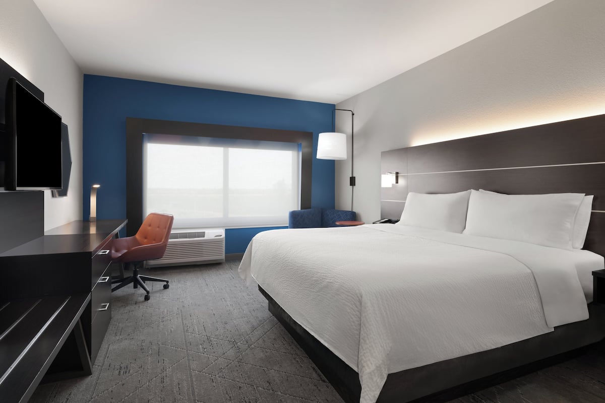 A hotel room with a large bed, a desk with a chair, a television, and a window with a view.