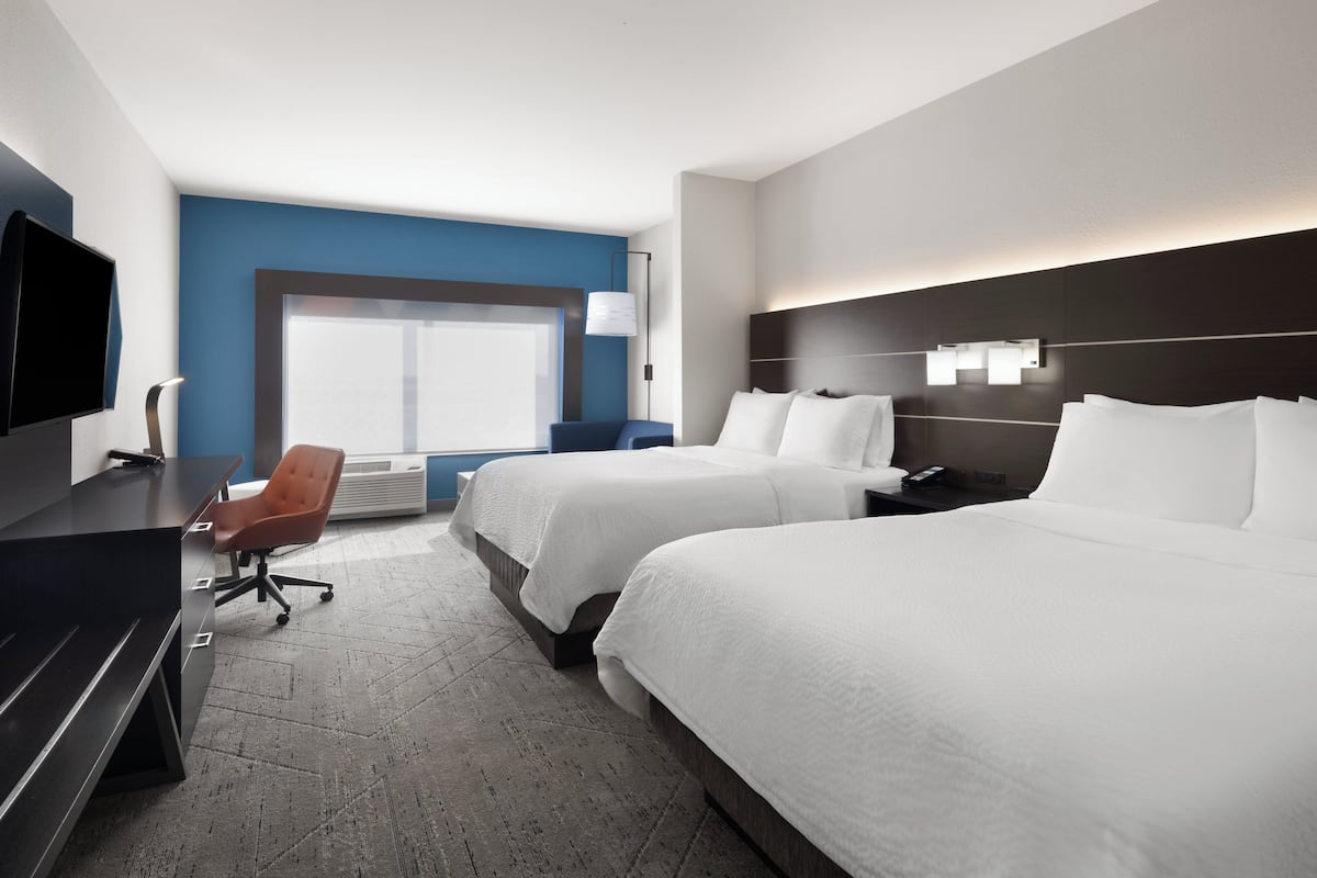A hotel room with two beds, a desk, a chair, a TV, and a window with blinds.