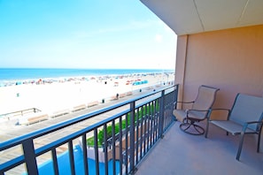 A balcony with a view of a beach, featuring a wooden deck and two chairs.
