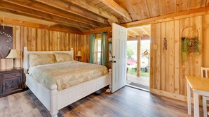 A wooden-paneled bedroom with a bed, bedside table, and a door leading to an outdoor area. - 'Wapiti' Allenspark Cabin Near Rocky Mountains! (Allenspark)