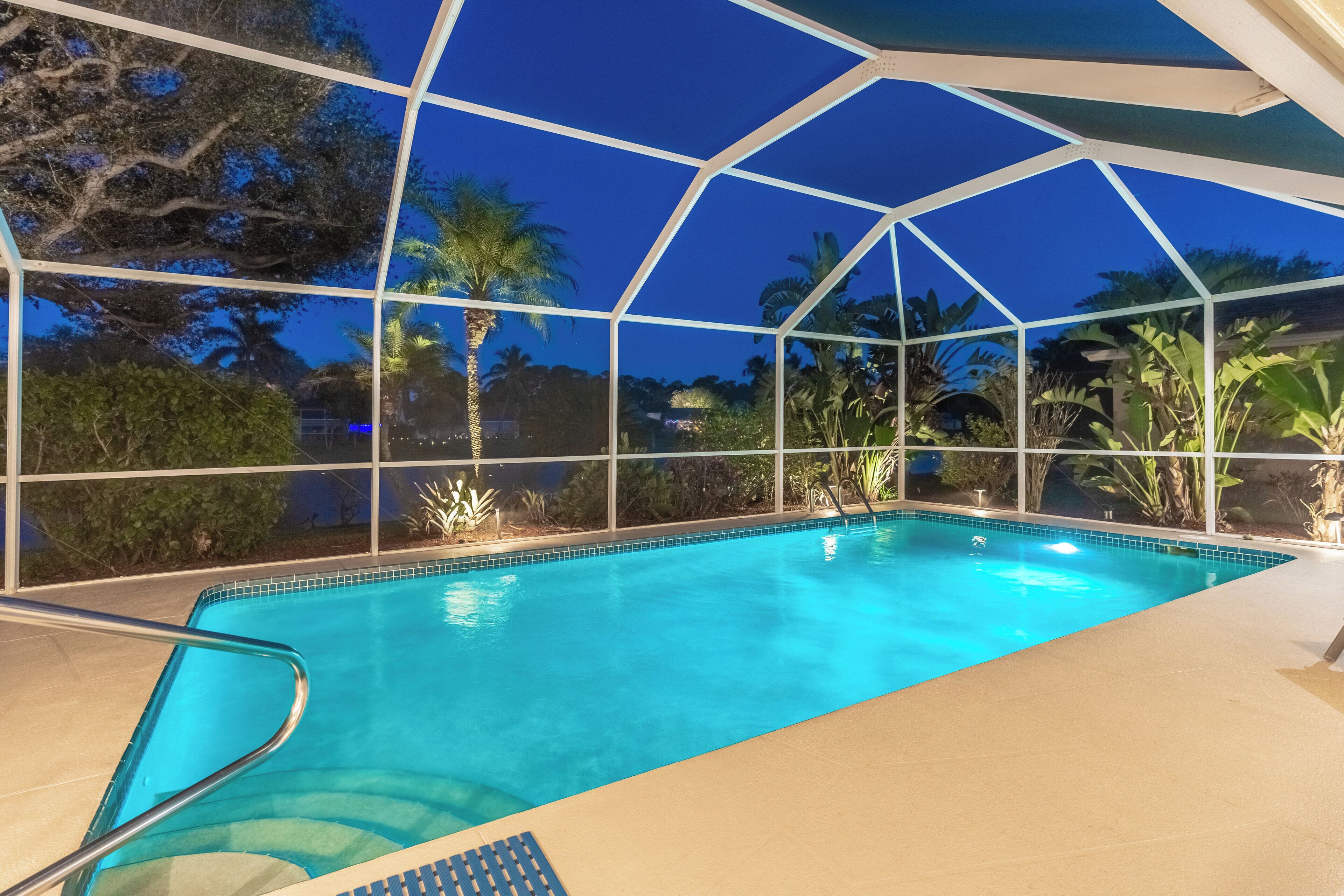 A clear blue pool with a glass enclosure, surrounded by tropical plants and trees.