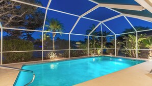 Una piscina azul cristalina con cerramiento de vidrio, rodeada de plantas y árboles tropicales.