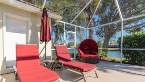 Un espacio al aire libre techado con dos sillones rojos y una silla de mimbre, una sombrilla roja, y vistas a un lago y árboles.