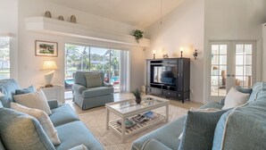 Amplia sala de estar con televisor grande, asientos cómodos y vista al exterior.