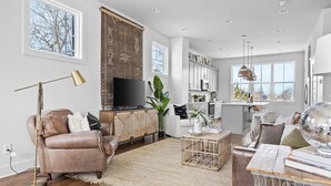 A spacious living room with a leather sofa, a television, and a large window.
