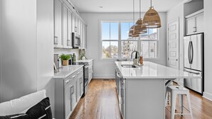 A modern kitchen with white cabinetry, stainless steel appliances, and a large window providing natural light.
