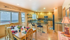 Una cocina amplia con armarios de madera, una isla central y un comedor con una mesa dispuesta para cuatro.