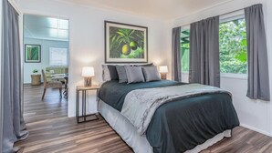 Une chambre à coucher avec un lit, deux tables de chevet, un tableau encadré et une fenêtre avec des rideaux.