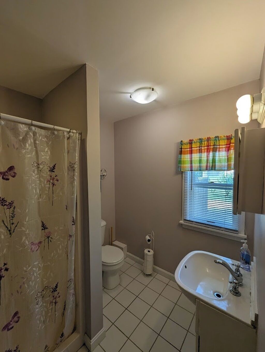 Een badkamer met toilet, wastafel, douche en een raam met zonwering.