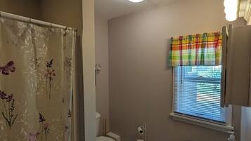 Een badkamer met toilet, wastafel, douche en een raam met zonwering.