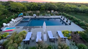 A rectangular pool with two separate sections, surrounded by lounge chairs and a colorful mat.
