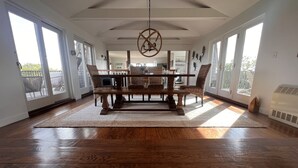 A spacious dining area with a wooden table and chairs, large windows, and a ceiling fan.