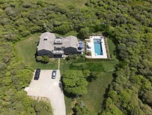An aerial view of a house with a swimming pool, surrounded by dense greenery.