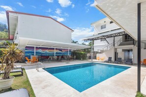 Una piscina con sillas de descanso, un mural y una zona de estar cubierta al aire libre.