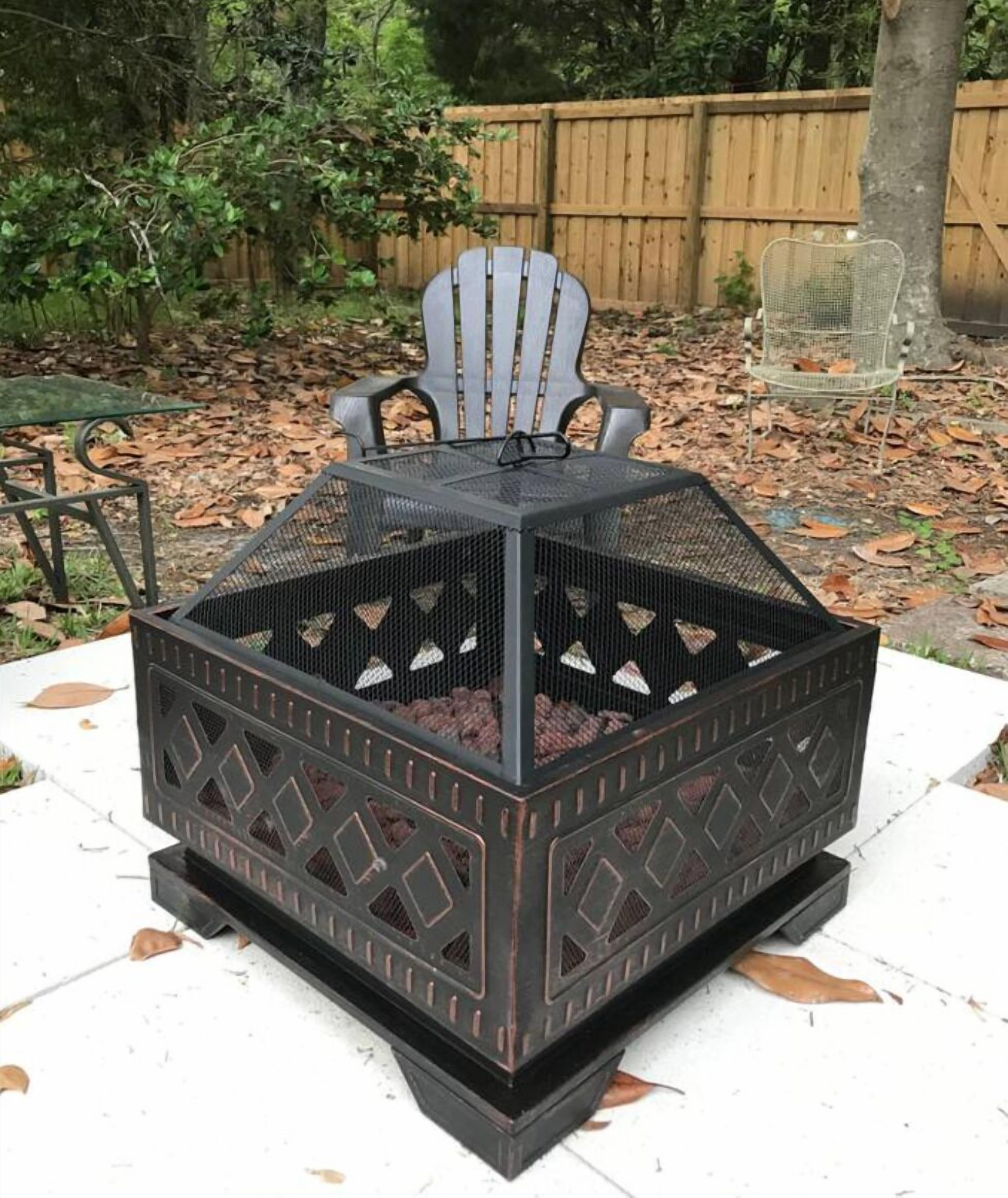 A metal fire pit with a metal chair on top, surrounded by a wooden fence and trees.