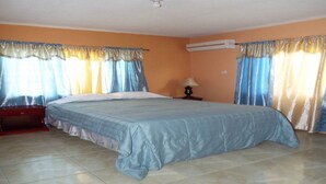 A bedroom with a bed, curtains, a nightstand, and an air conditioning unit. - BPO/Business Travellers/ Large Group Accommodation  (Spanish Town)