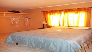A hotel room with a bed, a nightstand, a lamp, and a window with curtains. - BPO/Business Travellers/ Large Group Accommodation  (Spanish Town)
