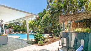 Ein Poolbereich mit Liegestühlen, einer Pergola und einer strohgedeckten Struktur.