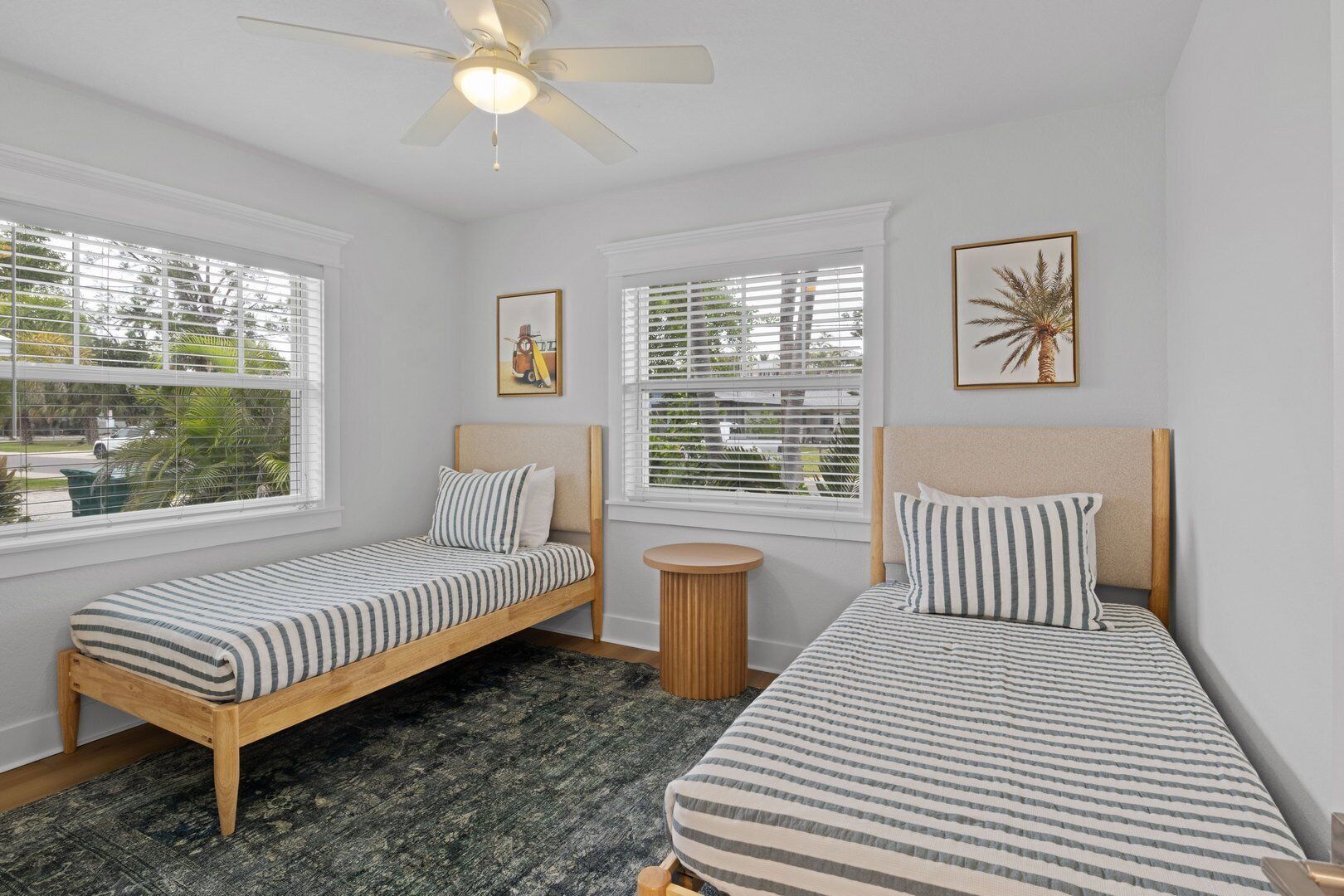A bedroom with two single beds, a ceiling fan, and large windows with blinds.