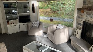 Un salon avec une cheminée, une table basse en verre et un ensemble de canapés.