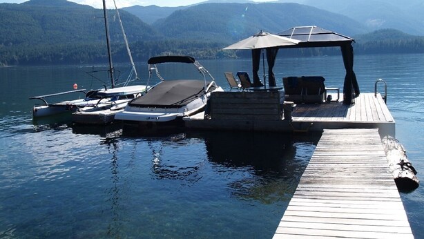 Un quai avec des bateaux et un espace de repos couvert, donnant sur un lac avec des montagnes en arrière-plan.