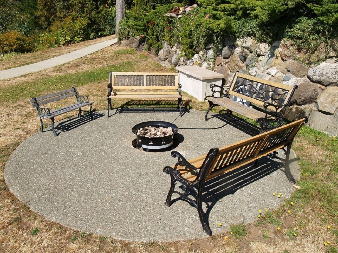 A circular outdoor seating area with three wooden benches and a fire pit.