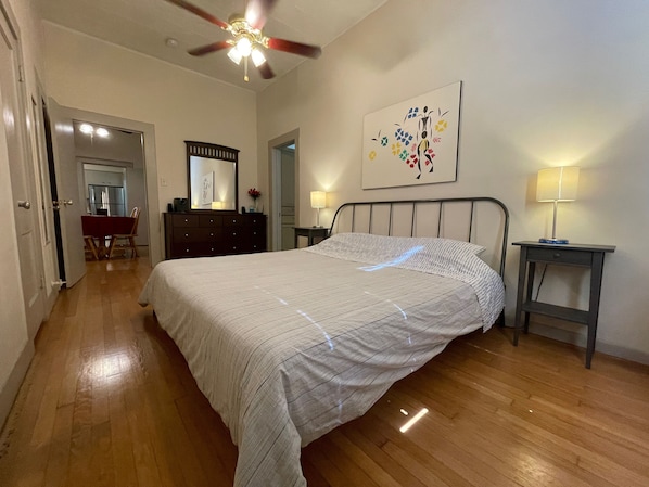 A bedroom with a bed, a dresser, a desk, a chair, a ceiling fan, and a wall-mounted lamp.