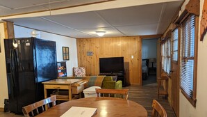 Un salon chaleureux avec une table à manger en bois, un réfrigérateur noir et un téléviseur.