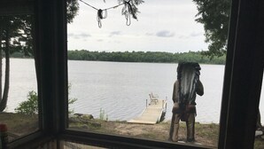 Vue sur un lac, prise de l’intérieur d’un chalet doté d’une jetée et d’un banc.