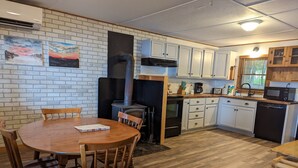 Une cuisine avec des meubles blancs, un poêle à bois et un coin repas comprenant une table et des chaises en bois.