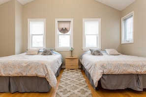 A bedroom with two beds, a nightstand, and a window with blinds.