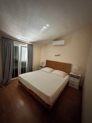 Een slaapkamer met een groot bed, twee nachtkastjes met lampen, een plafondairconditioner en een schuifglazen deur met gordijnen.